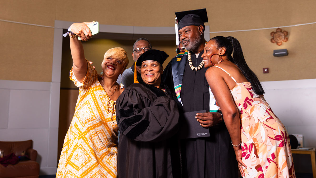 man in graduation cap and gown, with woman in doctoral regalia, and three other people